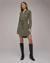 Woman in a Bella Dahl TENCEL™ Lyocell Flap Pocket Shirt Dress in Herb Green and black knee-high boots standing against a neutral background.