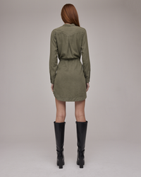 Woman standing with her back to the camera wearing a green Bella Dahl TENCEL™ Lyocell flap pocket shirt dress in Herb Green and black knee-high boots.