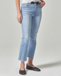 A person wearing light blue, mid rise, Citizens of Humanity Isola Cropped Boot in Marquee jeans with frayed hems and black flats.