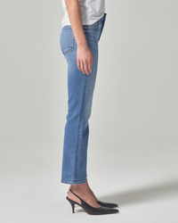 A person standing side-on wearing blue Citizens of Humanity mid-rise jeans and a white top with black heels.