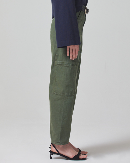 Sentence with replaced product: Person standing sideways wearing Citizens of Humanity Marcelle Low Slung Cargo in Surplus Sateen made from organic cotton and non-stretch twill, paired with black strappy sandals.