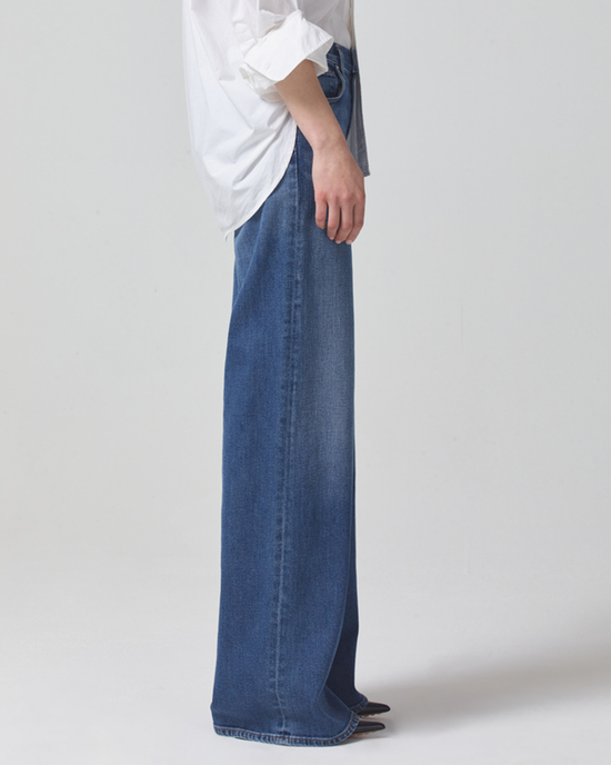 A person standing sideways wearing a white shirt and blue Citizens of Humanity Loli Mid Rise Baggy in Palazzo wide leg flared jeans.