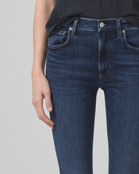 Close-up of a person wearing Citizens of Humanity Sloane Skinny w/ Clean Hem in Baltic jeans with a black top, standing with one hand touching their thigh.