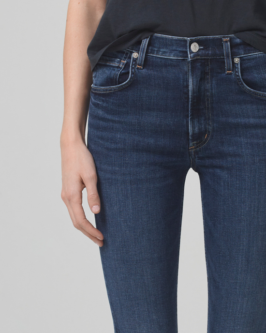 Close-up of a person wearing Citizens of Humanity Sloane Skinny w/ Clean Hem in Baltic jeans with a black top, standing with one hand touching their thigh.