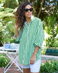 A woman wearing sunglasses and the Frank & Eileen Shirley Oversized Button Up Shirt in Wide Green Stripe, woven in Italy, standing in a garden setting.