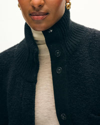 A person wears the White + Warren Boucle Blend Luxe Jacket in Black, featuring a high ribbed collar, over a cream turtleneck sweater, styled with visible gold hoop earrings.