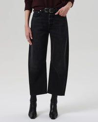 A person wearing Citizens of Humanity’s Miro Relaxed Jean in Raine, styled with a belt, black boots, and a dark long-sleeve top, stands against a white background. Only the lower torso and legs are visible.