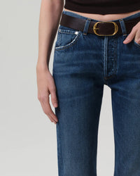 A person wearing Citizens of Humanity Winslow Low Rise Boyfriend jeans in Tinsley, styled with a black belt with a large oval gold buckle and a dark sleeveless top, shown from waist to mid-thigh with one hand by their side.