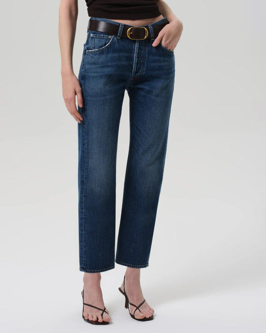 Someone wears Citizens of Humanity's Winslow Low Rise Boyfriend in Tinsley jeans—dark blue with a straight-leg boyfriend fit—paired with a black sleeveless top, black belt with gold buckle, and black strappy heeled sandals against a plain light background.
