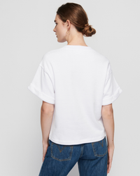 Woman wearing a white Nation LTD Bane Sweatshirt Tee and blue jeans, viewed from behind.