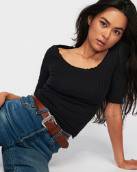 Woman posing in a Nation LTD Jezebel Scoop Neck w/ Merrow in Jet Black shirt and blue jeans with a brown belt.