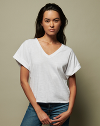 Woman in Nation LTD's Stevie Cuffed V Neck in White t-shirt made of 100% cotton Japanese Jersey and jeans standing against a neutral background.