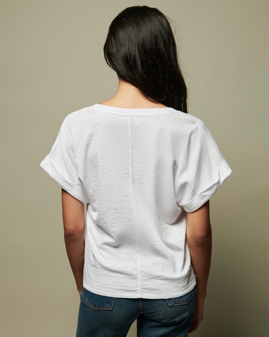 Woman standing with her back to the camera, wearing a white Nation LTD Stevie Cuffed V Neck t-shirt and blue jeans against a neutral background.