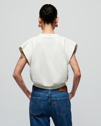 Woman seen from behind, wearing a Lenon Crewneck Sweatshirt in Porcelain by Nation LTD and blue jeans, with visible tattoos on her arms.