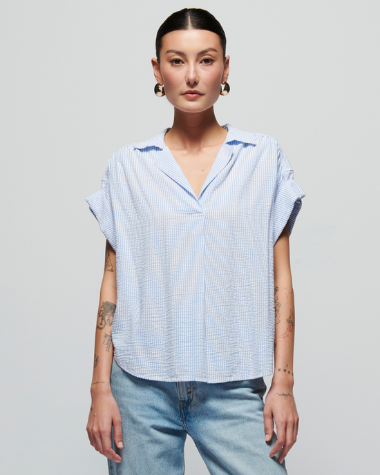 A woman with tattoos wearing a Nation LTD Elliott Stripe Shirt in Mini Stripe and jeans, standing confidently against a light gray background.