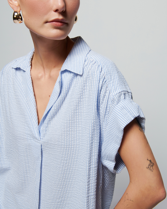 Close-up of a woman in a Nation LTD Elliott Stripe Shirt in Mini Stripe, showing the collared V-neck and sleeve detail, with a partial view of her face and a small tattoo on her arm.