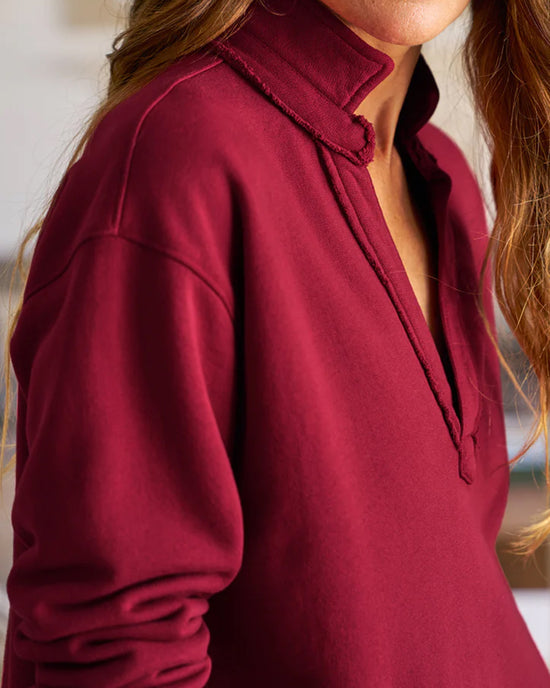 A person with long, wavy hair wears the Frank & Eileen Patrick Popover Henley in Garnet French Terry, featuring a split V-neck and raw edge collar, with a softly blurred background highlighting the upper part of the outfit.