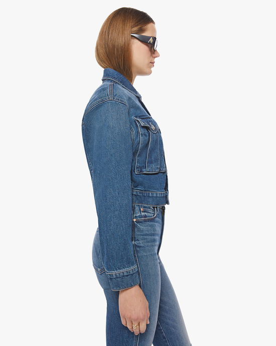 Profile view of a woman wearing a Mother Out Of Pocket Jacket in Morning Chores denim jacket and jeans with sunglasses.