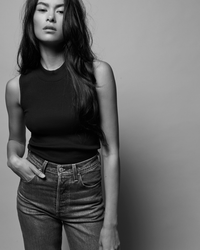 Woman in a Joan Sleeveless Mock Neck in Jet Black top from Nation LTD and jeans posing with hand in pocket against a plain background.