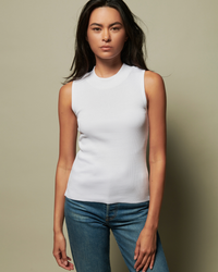 Woman in a Nation LTD Joan Sleeveless Mock Neck in White top and blue jeans against a neutral background.