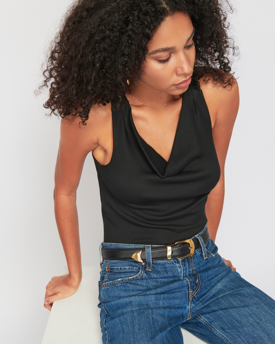 Woman in black Nation LTD Tarin Racerback Cowl in Jet Black top and jeans sitting and looking down.
