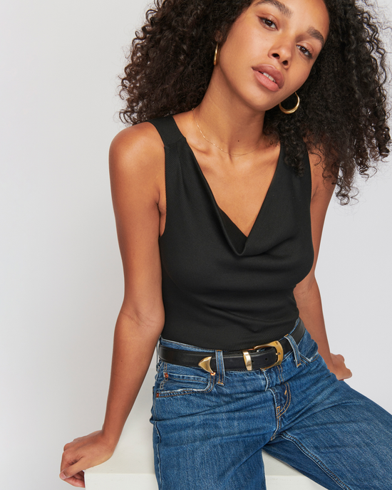 A woman in a Nation LTD Tarin Racerback Cowl in Jet Black and blue jeans with a belt posing for the camera.