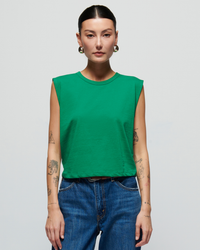 Woman in a Nation LTD Collins Crewneck Solid Tank in Verdant Green and high-rise denim jeans, with tattoos on her arms, standing against a light background.