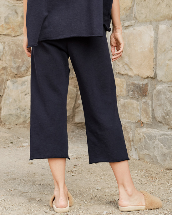 A person wearing black Frank & Eileen Catherine Sweatpant in British Royal Navy and beige flat shoes standing against a stone wall, all Made in the USA.
