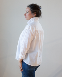 Woman standing in profile wearing a CP Shades Joey Short Shirt in White Cotton Oxford with button-front closure and jeans.