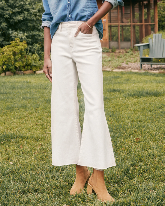 A person standing on grass, wearing white Frank & Eileen Galway Gaucho in Natural Denim jeans and tan ankle boots.
