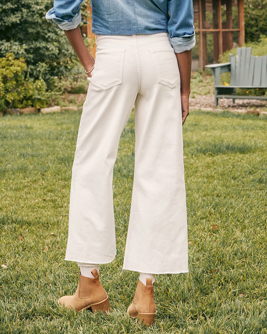 A person standing in a garden wearing Frank & Eileen's Galway Gaucho in Natural Denim jean pants and tan ankle boots, with a blue denim shirt tucked in at the waist.