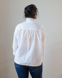 A person seen from behind wearing a CP Shades Joey Short Shirt in White Cotton Oxford with a button-front closure and blue jeans.