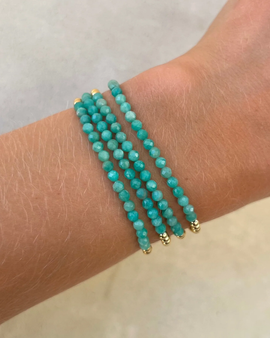 A wrist adorned with three strands of Karen Lazar Design 3MM Sig Bracelet with Amazonite & Yellow Gold bracelets, interspersed with 14k Yellow Gold filled beads.