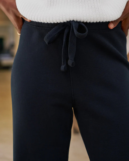 Close-up of a person wearing Frank & Eileen's Catherine Long Sweatpant in British Royal Navy and a white ribbed sweater, hands on hips.