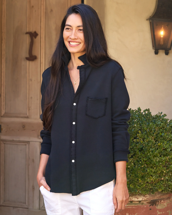 A smiling woman standing in front of a door, wearing a Frank & Eileen Eileen Relaxed Button Up in British Royal Navy Triple Fleece shirt and white pants.