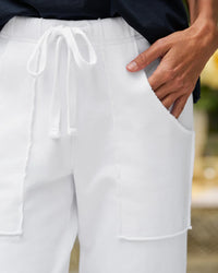Wearing Frank & Eileens Penny Patch Pocket Sweatpant in White, with visible seams, large patch pockets, and a white drawstring, a person rests one hand in a pocket and pairs it with a dark top.