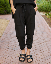 Woman wearing black Eamon Jogger Sweatpants by Frank & Eileen and black sandals standing on a brick pathway.