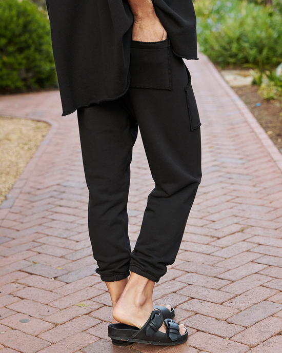 Person wearing black Eamon Jogger Sweatpants by Frank & Eileen and sandals standing on a brick pathway.