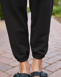 Close-up of a person wearing Frank & Eileen Eamon Jogger Sweatpants in Black and sandals.