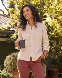Woman smiling and holding a mug in a sunny garden setting, wearing a Frank & Eileen Barry Button Up in Vintage White Cotton.