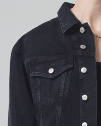 Close-up of a person wearing a black organic cotton Citizens of Humanity Dulce Denim Jacket in Venetia with silver buttons.