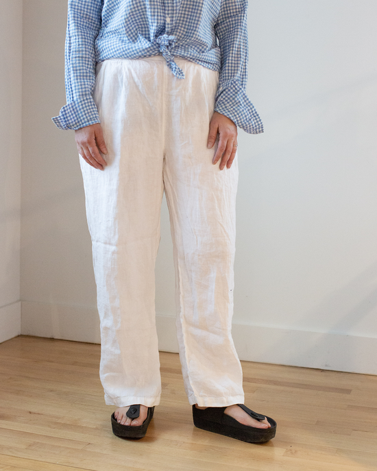 Person standing in CP Shades Tess Pant HW Linen Twill in White and dark sandals, wearing a blue and white checkered shirt tied at the waist.