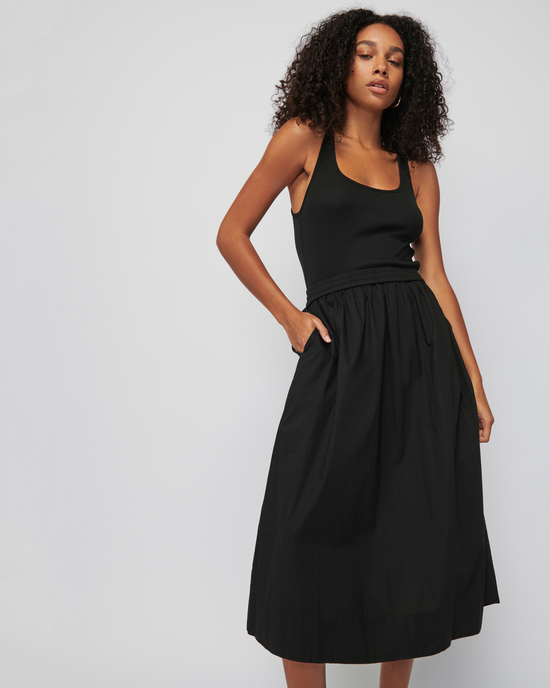 Woman posing in a sleeveless, racerback Sadelle Clean Combo Midi dress by Nation LTD and black midi skirt with an elastic waist.