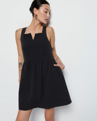 A woman with tattoos posing in a black Solie Dress in Jet Black by Nation LTD against a white background.
