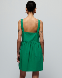 Woman seen from behind wearing a Nation LTD Solie Dress in Verdant Green with a square notch neckline, featuring visible tattoos on her arms and neck.