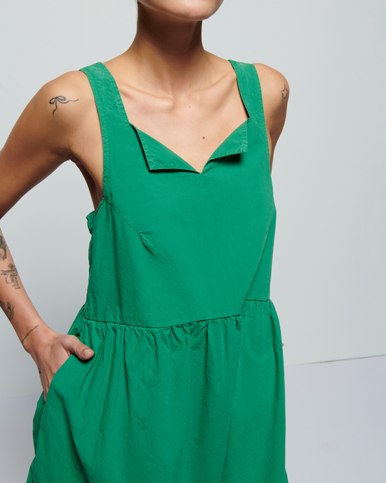 A person in a Nation LTD Solie Dress in Verdant Green with shirring around the waist, standing against a light background, with visible tattoos on the arms.