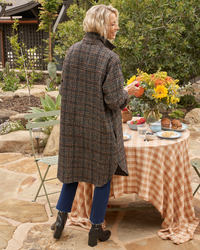 A woman in a Frank & Eileen Gavin Italian Wool Shirt Jacket in Black & Blue Textured Plaid arranging a bouquet of sunflowers on an outdoor dining table.