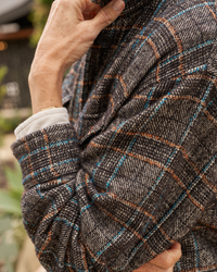 A close-up of a person's arm showing a hand holding the fabric of an oversized Gavin Italian Wool Shirt Jacket in Black & Blue Textured Plaid by Frank & Eileen with a visible cuff of a white shirt.
