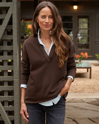 A woman standing outdoors wearing a brown 100% Cotton Fleece sweater and jeans with a Frank & Eileen Patrick Henley in Irish Chocolate Terry collared shirt underneath.