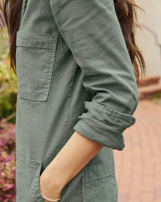 Close-up of a woman's side, focusing on her arm in a rolled-up sleeve of a green Frank & Eileen Ireland L/S Playsuit in Rosemary with a visible pocket.
